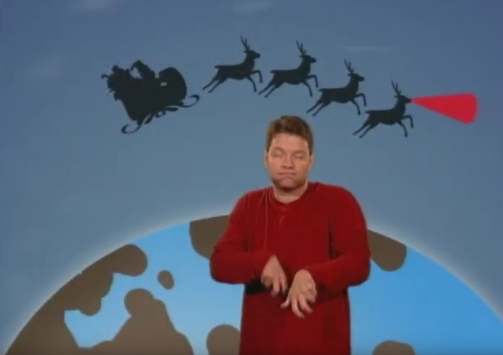 man signing in front of a cartoon image of the earth with Santa Claus and reindeer flying